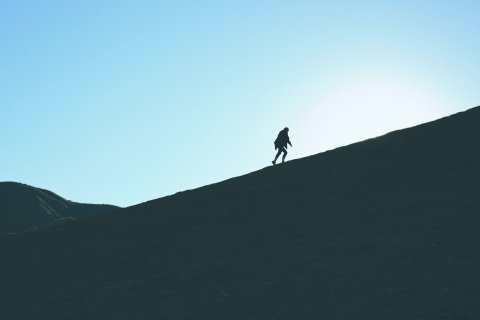 Backlit photo of a person walking up a mountain slope