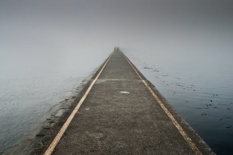 Photo of a road surrounded by water, going into the mist