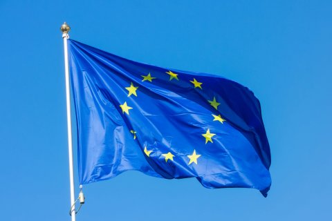 Drapeau de l'Union européenne bleu avec étoiles jaunes flottant sous un ciel bleu clair.