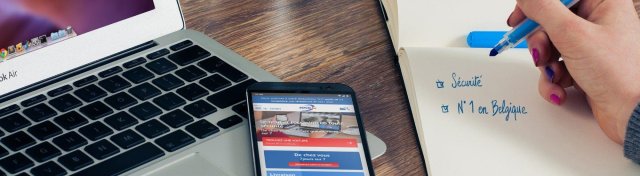 Téléphone avec la page soco.be ouverte et que main qui note dans un carnet