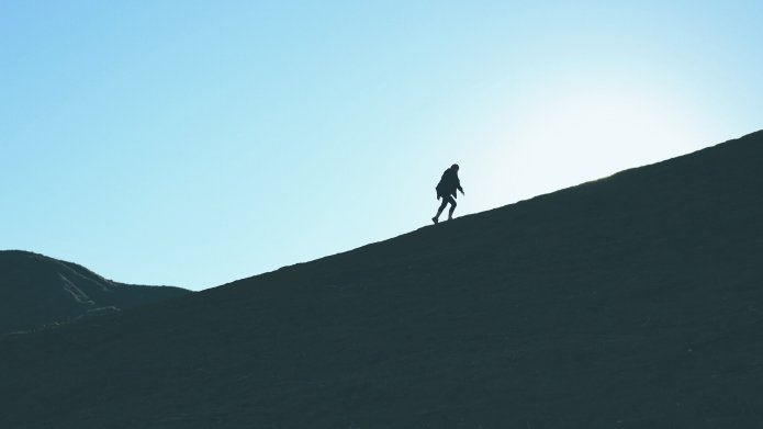Backlit photo of a person walking up a mountain slope