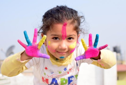 Petite fille souriante avec les mains et le visage couverts de peinture colorée.