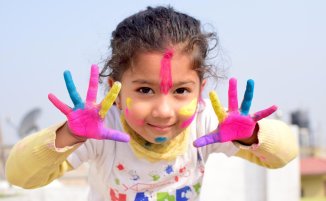 Petite fille souriante avec les mains et le visage couverts de peinture colorée.