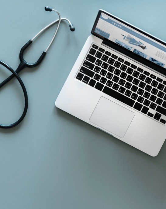 un pc un stéthoscope, une paire de lunette et un cahier posé sur un plan de travail